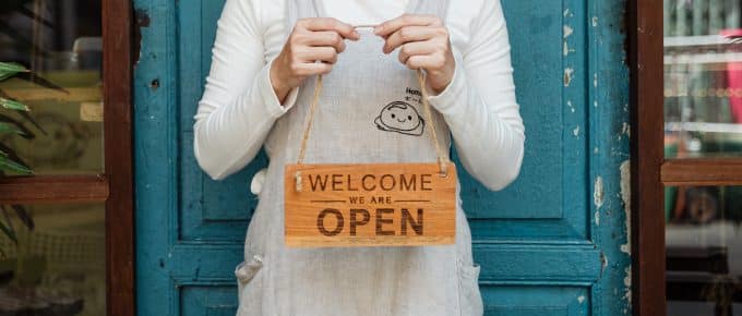 small business owner holds a "we are open" sign